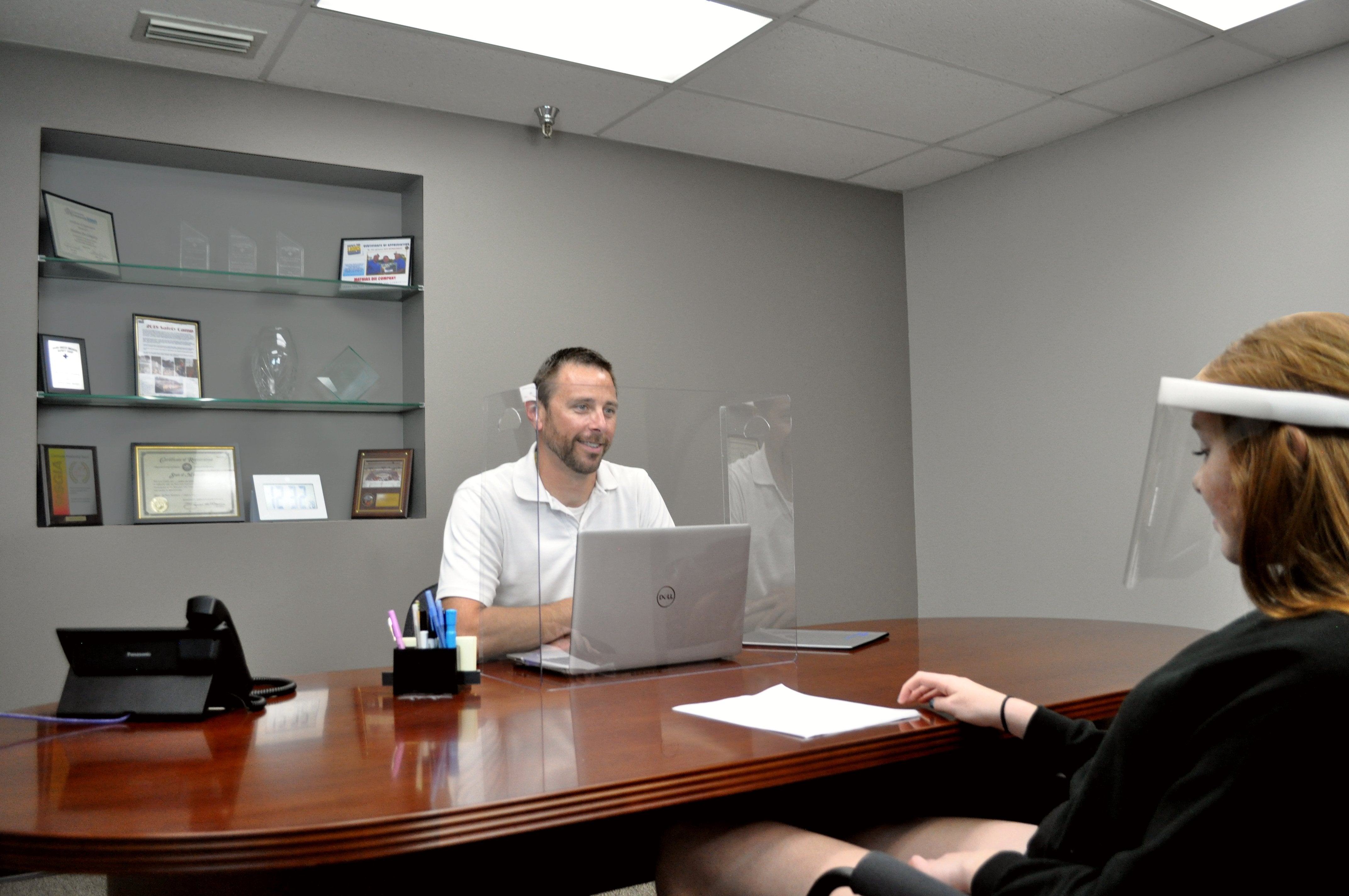 A man sitting at a desk with a laptop behind a Table Shield while talking to a woman wearing a ComfaShield.